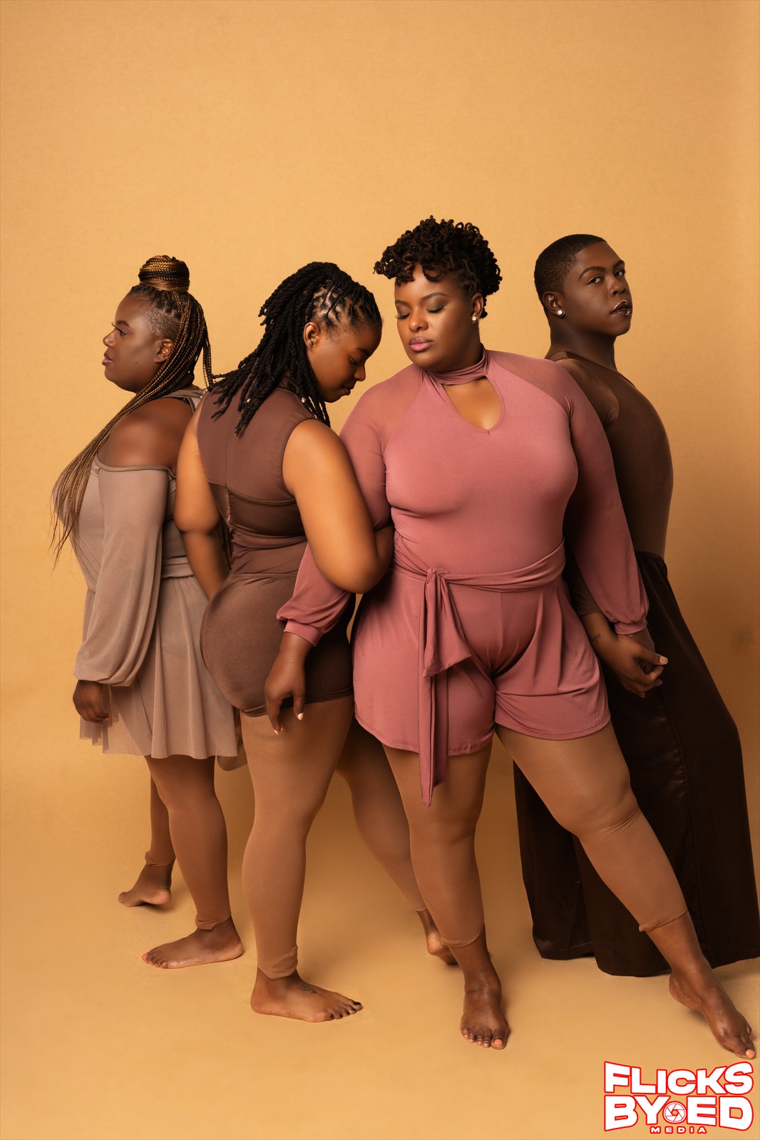 Four people posed together in coordinated earth-tone outfits against a warm gold studio backdrop.