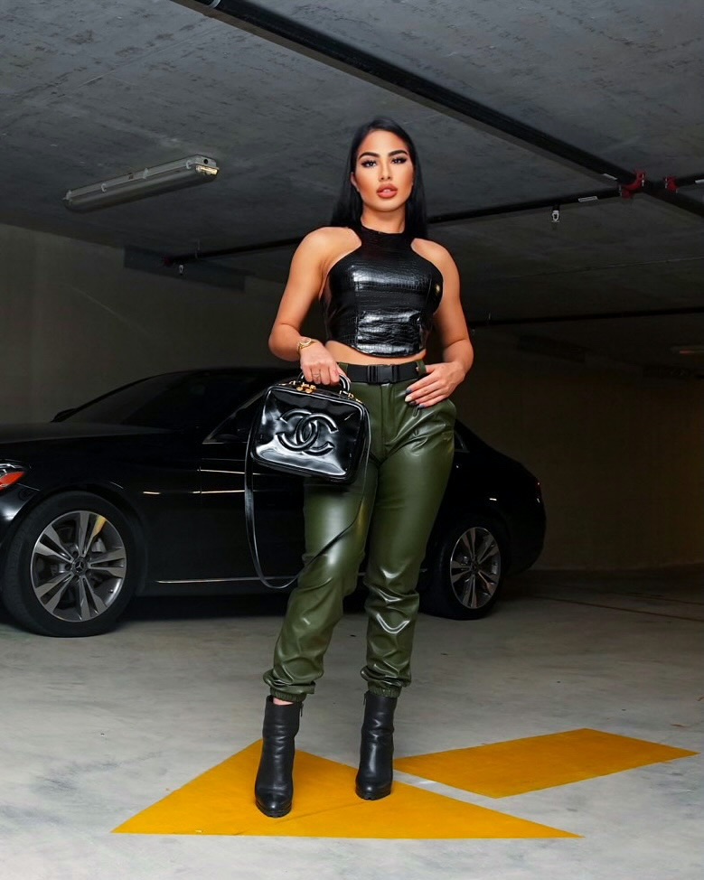A fashion portrait in a black top and olive trousers, standing above a yellow floor arrow in a parking garage.